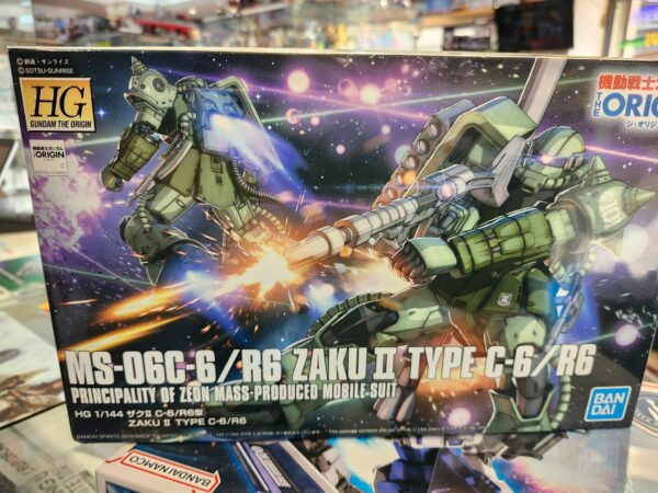 Photographie de la boîte de maquette Bandai Namco High Grade (HG) issue de Gundam The Origin, représentant le mobile suit de série MS-06C-6/R6 Zaku II Type C-6/R6 de la Principauté de Zeon en position de combat avec son armement.