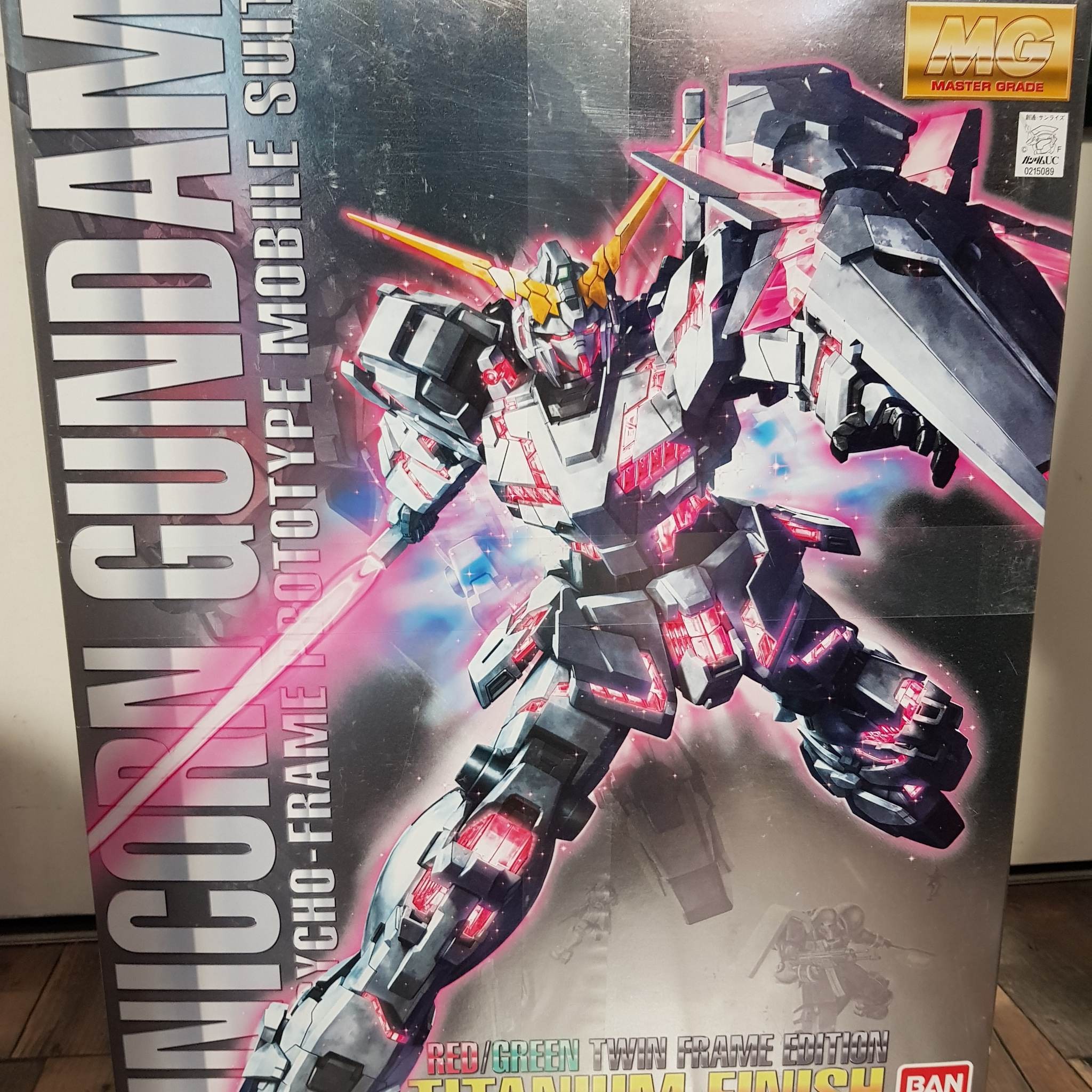 Photographie de la boîte de maquette représentant le MG Unicorn Red/Green Twin Frame Edition Titanium, un modèle Gundam collector au design rouge et vert.